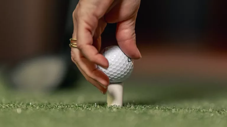 En hand placerar en golfboll på en peg på konstgräs.