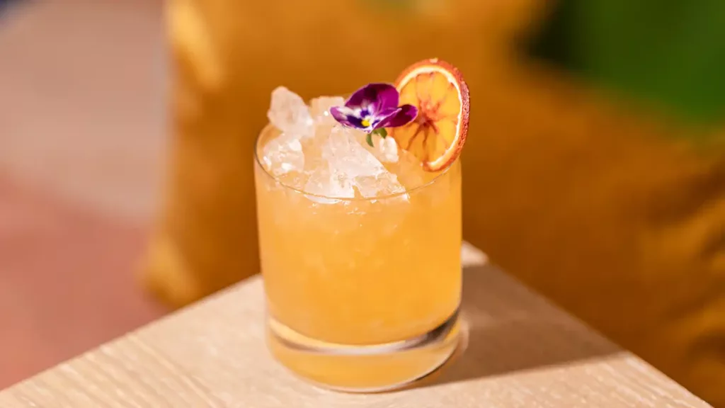 Gulorange cocktail med krossad is, torkad citrus och ätbar blomma – serverad på Pachanga pool club & spa i Göteborg.